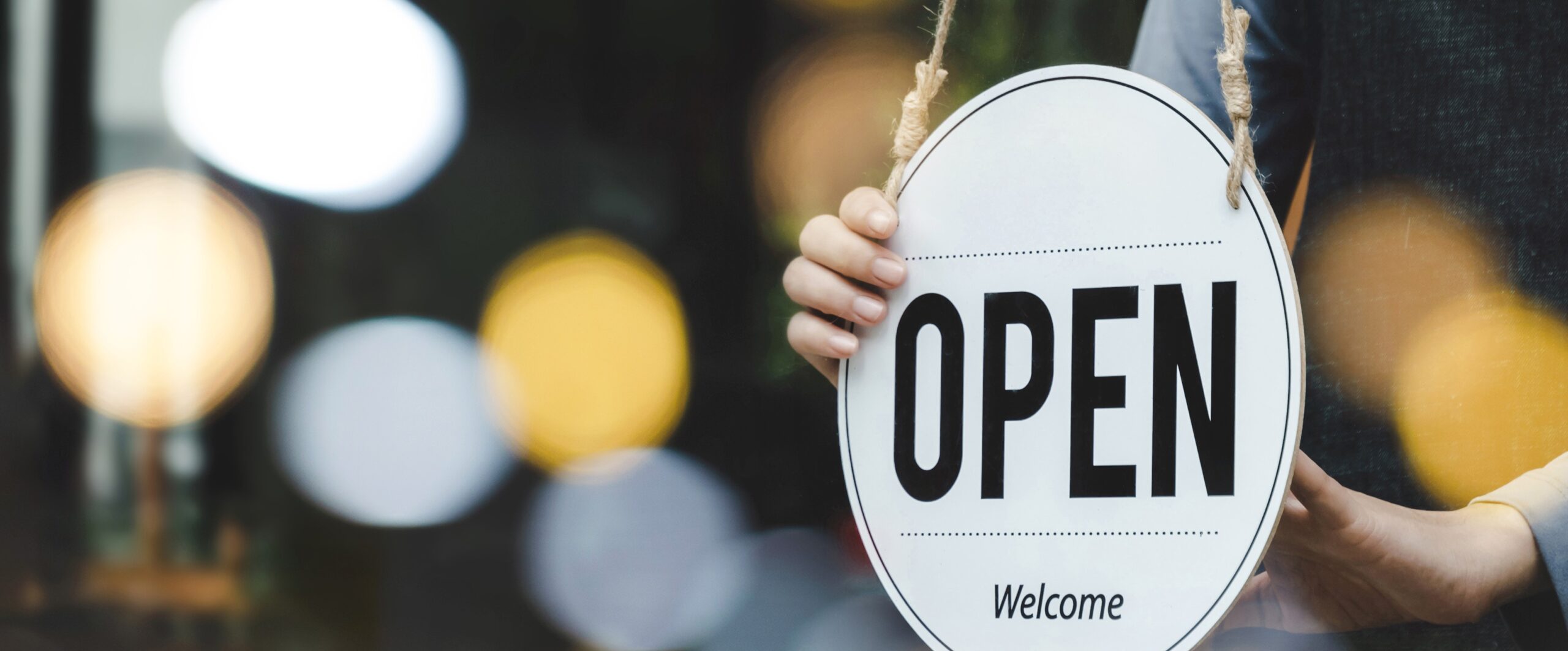 Welcome. waitress staff woman turning wooden open sign board on glass door with bokeh ligh in modern cafe coffee shop, cafe restaurant, retail store, small business owner, food and drink concept